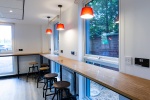 Modern dining room with high table and chairs, bright windows. Space for meals or study.