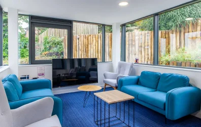 Modern common room at Goods Corner in Edinburgh with blue and grey furniture, garden views, and vari
